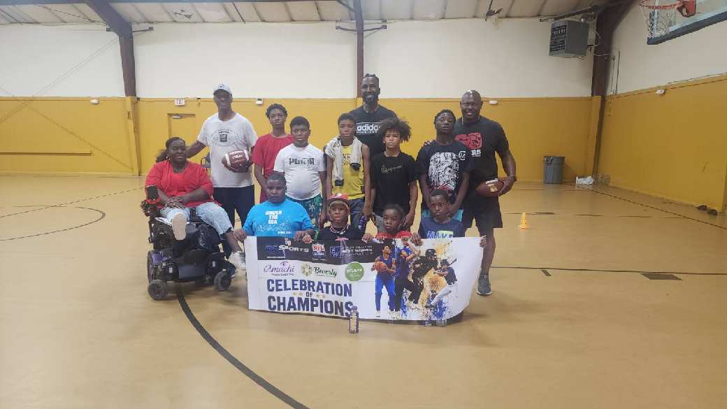 Young athletes and mentors posing with a Celebration of Champions banner in a gym