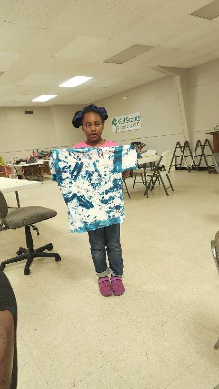 Girl Scout proudly holding up a blue and white tie-dye shirt
