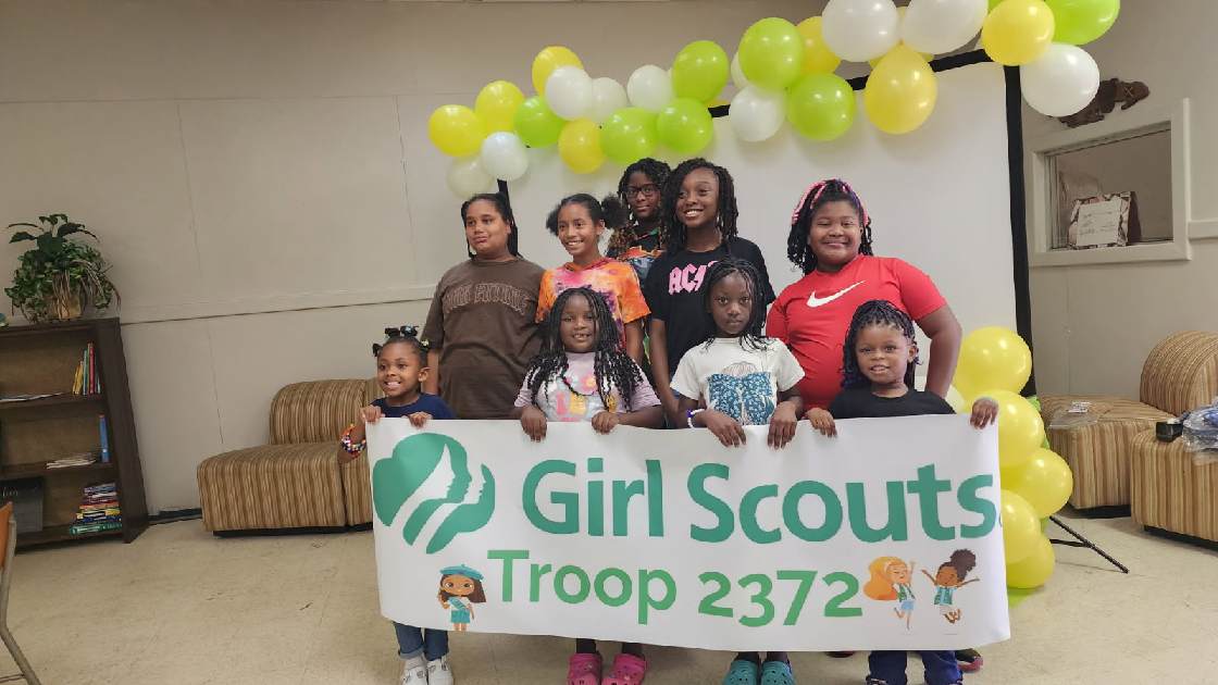 Girl Scout troop gathered beneath balloons with their troop banner