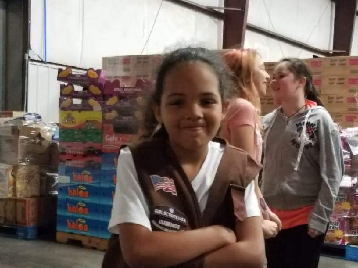 Girl Scout volunteering near donated supplies in a warehouse