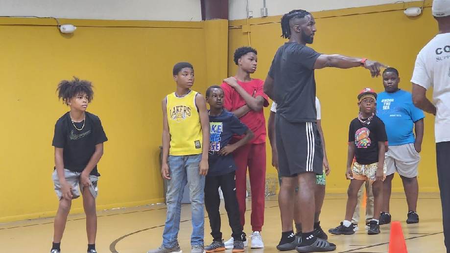 A coach giving instructions to young athletes during a gym activity